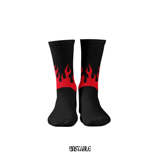 A pair of black socks with red flame designs, placed against a grey background. The socks are marked with the word 'UNSTABLE'.